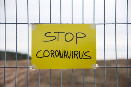 STOP CORONAVIRUS text on the yellow plate on a mesh wire fence. Quarantine Area COVID-19. Outbreak...