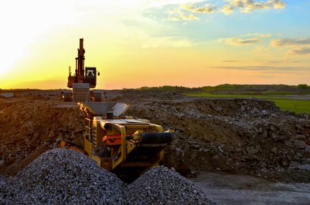 Excavator in a mining quarry at sunset. Mobile Stone crusher machine by the construction site or...