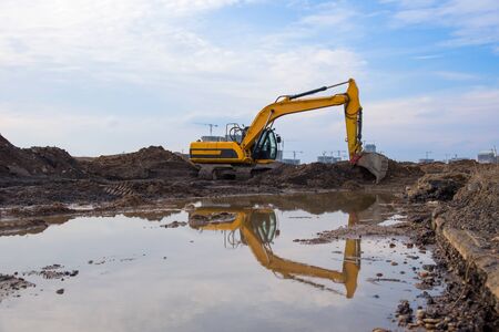 Excavator at lake in the quarry on sunset background. Backhoe during earthmoving work at open-pit...