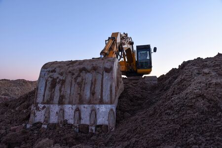Excavator during earthmoving work at open-pit mining on sunset background. Loader machine with...