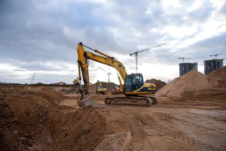 Excavator during earthmoving at construction site. Backhoe dig ground for the construction of foundation and laying sewer pipes district heating. Earth-moving heavy equipment on road worksの写真素材