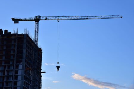 Tower crane in action on blue sky background. Preparing to pour a bucket of concrete into formwork....