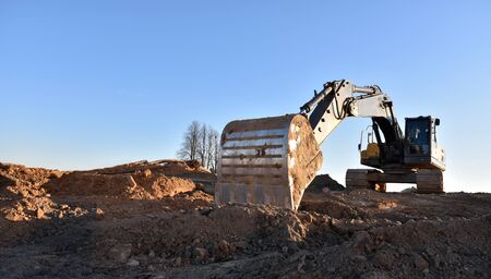 Yellow excavator during earthmoving at open pit on blue sky background. Construction machinery and...