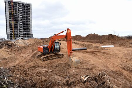Red excavator during earthmoving at construction site. Backhoe dig ground for the construction of...
