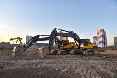 Group of the excavators for digging ground, trenching and foundation at construction site. Backhoe on blue sky background during sunset. Earth-moving heavy equipmentの写真素材