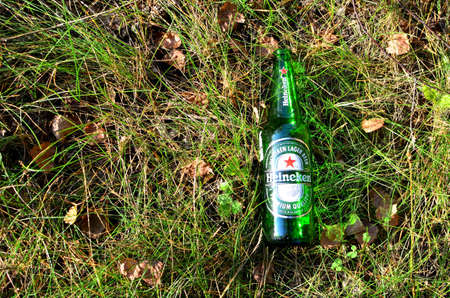 18.09.2019 Minsk, Belarus: Heineken Lager Beer  glass bottle on green grass. People throw food waste, leave trash on the street after themselves. The concept of the social problem of alcoholism.のeditorial素材