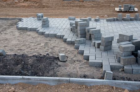 Laying paving slabs and borders at construction site. Process of installing paving bricks in the town pedestrian zone. Screeding the sand for install concrete blocks. Road works on pavement renovationの写真素材