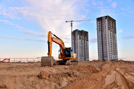 Excavator and tower crane at construction site on sunset background. Cranes constructing a new...