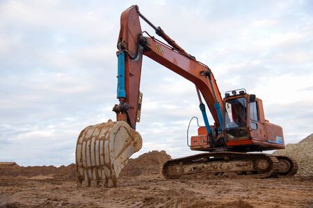 Excavator working on earthmoving at open pit mining. Backhoe digs gravel in quarry. Construction machinery for excavation, loading, lifting and hauling of cargo on job sitesの写真素材