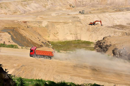 Dump truck transports sand in open pit mine. Excavator in quarry excavate from ground which sand and...