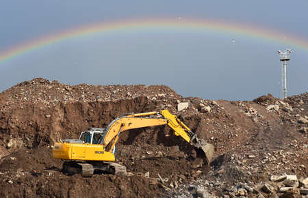 Excavator at landfill on rainbow background in sky. Disposal of construction waste and concrete...