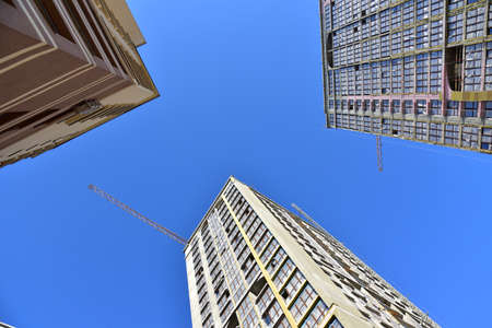 Tower cranes working at construction site on blue sky background. Construction process of the new...