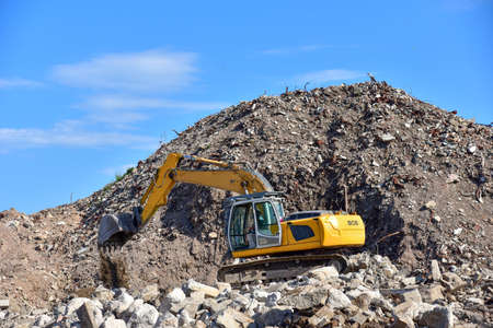 Yellow excavator at landfill for disposal of construction waste. Backhoe dig gravel at mining quarry...