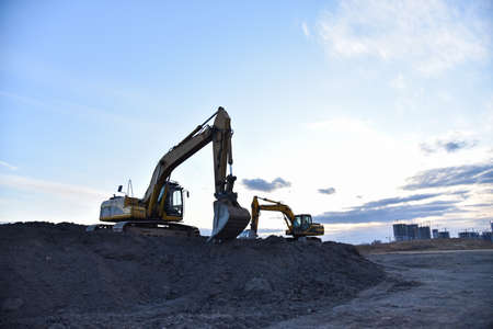 Excavators work at constrruction site on sunset background. Backhoe digs gravel and old concrete....