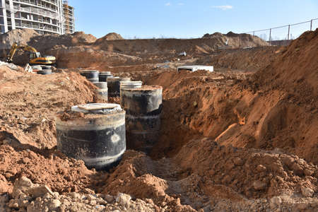 Laying concrete manholes and heating drain pipes and for stormwater system in trench at construction site. Sewerage manhole and pipes line under construction. Chambers and Pump Stationの写真素材