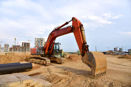 Large construction site with tower cranes and buildings on sunset background. Excavator during...