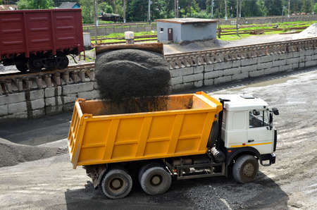 Wheel loader loads gravel into a dump truck at a cargo railway station. Fron-end loader unloads...