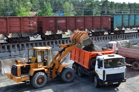 Wheel loader loads gravel into a dump truck at a cargo railway station. Fron-end loader unloads...