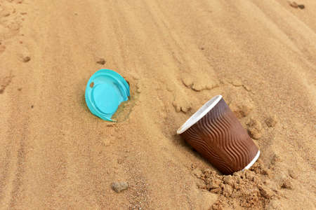 Discarded Paper coffee cup on sand at beach. Disposable coffee cup on sandy background. The problem...