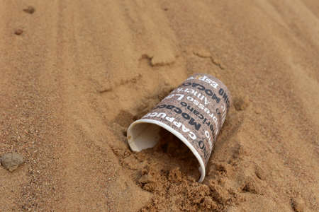 Discarded Paper coffee cup on sand at beach. Disposable coffee cup on sandy background. The problem...