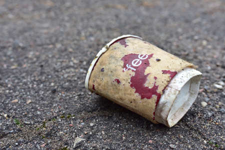 Crumpled a paper coffee cup on asphalt. Discarded disposable coffee cup with a plastic lid on road. Out of shape crushed paper cup. Abandoned garbage of disposable cups.の写真素材