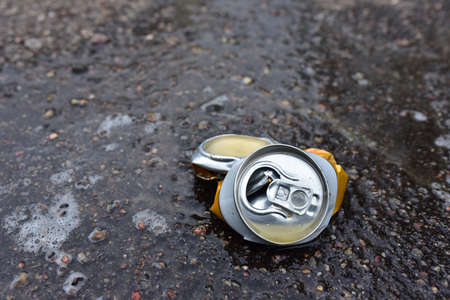 Crumpled a beer can on asphalt with spilled alcohol. Discarded broken carbonated drink can at a...