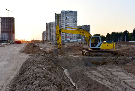 Excavator during excavation at construction site on sunset background. Red Backhoe on road work....