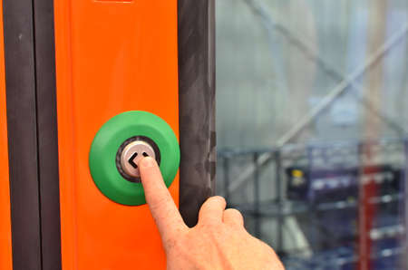 The hand presses the button for stop in the train. Orange door of train carriage with the electric...