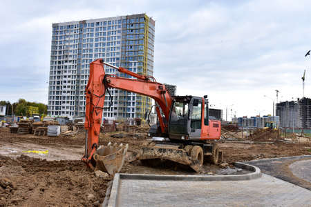 Bucket wheel excavator on earthmoving at construction site. Backhoe digs digs the ground to lay pipes and a new road. Tower cranes are building tall residential buildings. Renovation conceptの写真素材