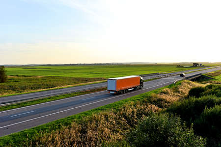 Truck with semi-trailer driving along highway on the sunset background. Goods delivery by roads. Services and Transport logistics. Soft focus. Object in motion.の写真素材