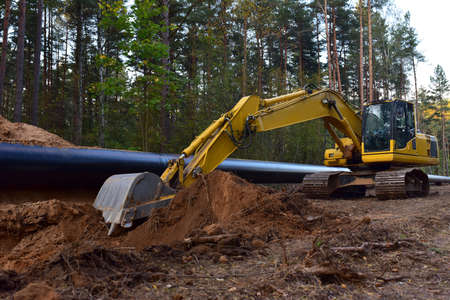 Excavator during earthwork for laying Crude oil and Natural gas pipeline in forest area. Installation of gas and crude oil pipes in ground. Construction of the gas pipes to new LNG plantの写真素材