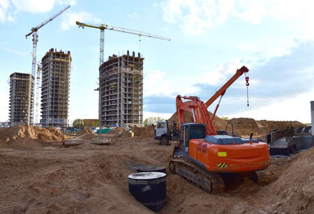Excavator on earthworks. Laying heating pipes and stormwater in trench. Installing concrete wells,...