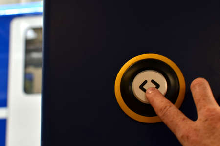The hand presses the button for stop in the train. Orange door of train carriage with the electric...