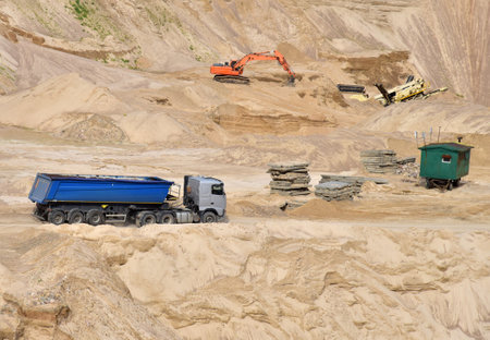 Truck with tipper semi trailer transported sand from the quarry. Dump truck and excavator working in open pit mine. Sand and gravel is excavated from ground. Mining industryの写真素材