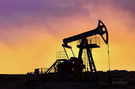 Crude oil pump jack at oilfield on atmospheric sunset backround. Fossil crude output and fuels oil production. Oil drill rig and drilling derrick. Global crude oil Prices, energy, petroleum demandの写真素材