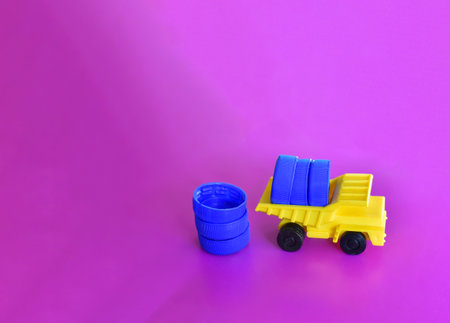 Toy dump truck unloads colorful plastic caps on on a lilac background. Concept for the collection, recycling of plastic bottle caps. Cap material is recyclable.の写真素材