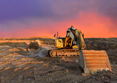 Excavator working on earthmoving at open pit mining on amazing sunset background. Backhoe digs sand...