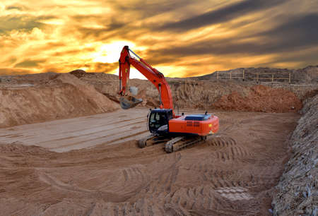 Excavator digging the pit foundation on sunset background. Earthwork in excavation and backfilling of soil is required for construction of trenche. Construction machinery for earthmovingの写真素材