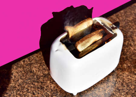 Burning toaster. Toaster with toast caught on fire over table.
