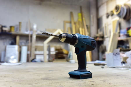 Cordless combi drill for used as impact drill and screw driver. Cordless impact screwdriver for work with self-tapping screws. Brushless battery drill on a wooden workbench in furniture workshopの写真素材