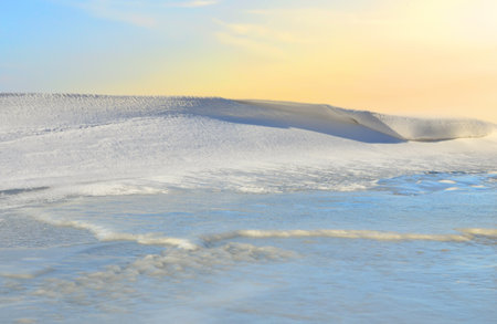 Structure of snow and ice on frozen lake on sunset background. Winter landscape concept. Frozen river surface view in winter timeの写真素材
