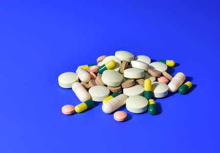 Pills and capsules on blue background. Medicine grade pharmaceutical tablets. Medical pill for maintaining and improving health. Antidepressant addiction and depression concept.の写真素材