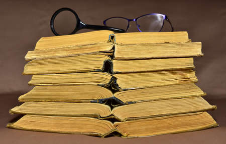 Glasses and magnifying glass on old books on brown background. Literature and historical concept, nostalgia, old age. Ancient historical mystical and magic books. Retro book. Reading stories.の写真素材