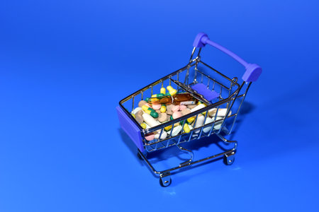Shopping cart with pills. Medicine grade pharmaceutical tablets and capsules in mini shopping trolley. Medical pill for maintaining and improving health. Financial and economic conceptの写真素材
