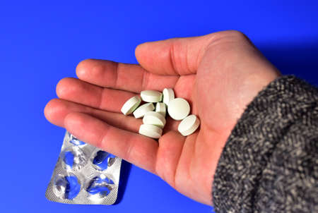 Pills in hand on blue background. Medicine grade pharmaceutical tablets. Medical pill for maintaining and improving health. Antidepressant addiction and depression conceptの写真素材