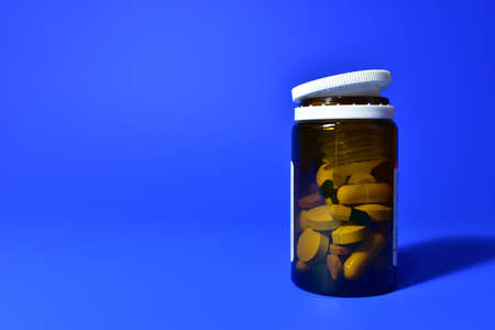 Pills in bottle on blue background. Assorted pharmaceutical pills, medical tablets and capsules. Medical pill for maintaining and improving health. Concept of healthcare and medicineの写真素材
