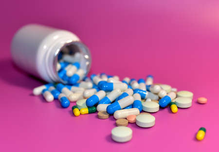 Pills from a bottle on pink background. Assorted pharmaceutical pills, medical tablets and capsules....