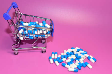 Pills in capsules and shopping cart. Medicine grade pharmaceutical tablets at mini shopping trolley. Medical pill for maintaining and improving health. Financial and economic conceptの写真素材