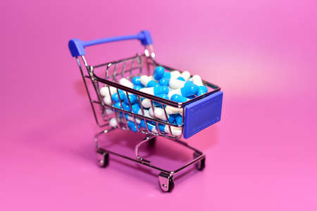 Pills in capsules and shopping cart. Medicine grade pharmaceutical tablets at mini shopping trolley. Medical pill for maintaining and improving health. Financial and economic conceptの写真素材