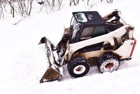 Skid-steer loader during snow removal on the road after a snowfall. Snow clearing is the job of...